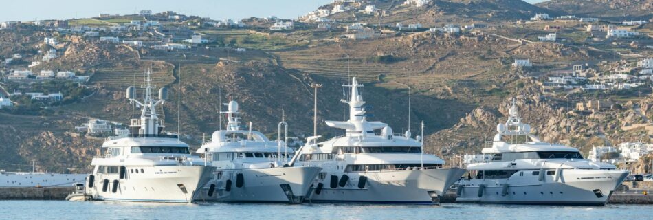 A row of luxury yachts moored at a picturesque harbor with hills in the background.