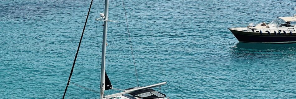 A serene view of a yacht and sailboats cruising in crystal clear turquoise waters near rocky cliffs.