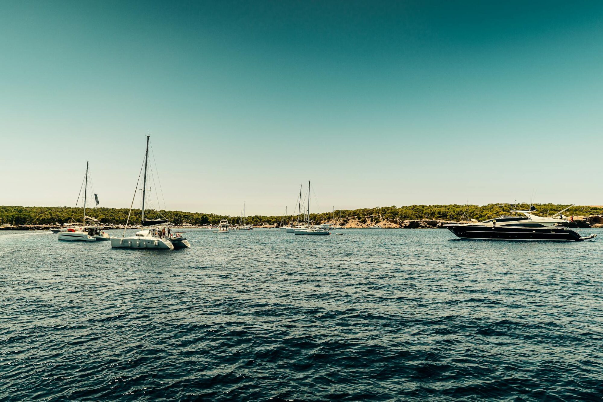 Picturesque scene of sailboats and yachts on Ibiza's clear waters under a bright summer sky.